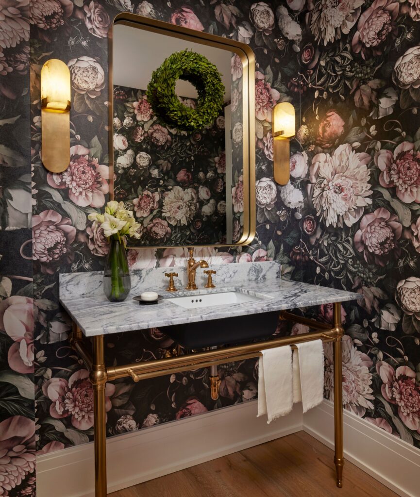 Moody floral bathroom wallpaper with gold mirror and warm lighting